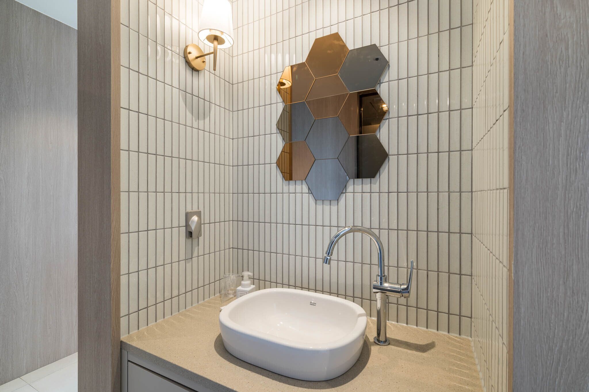 Une salle de bain moderne avec un lavabo blanc, un miroir et un motif géométrique sur le mur.