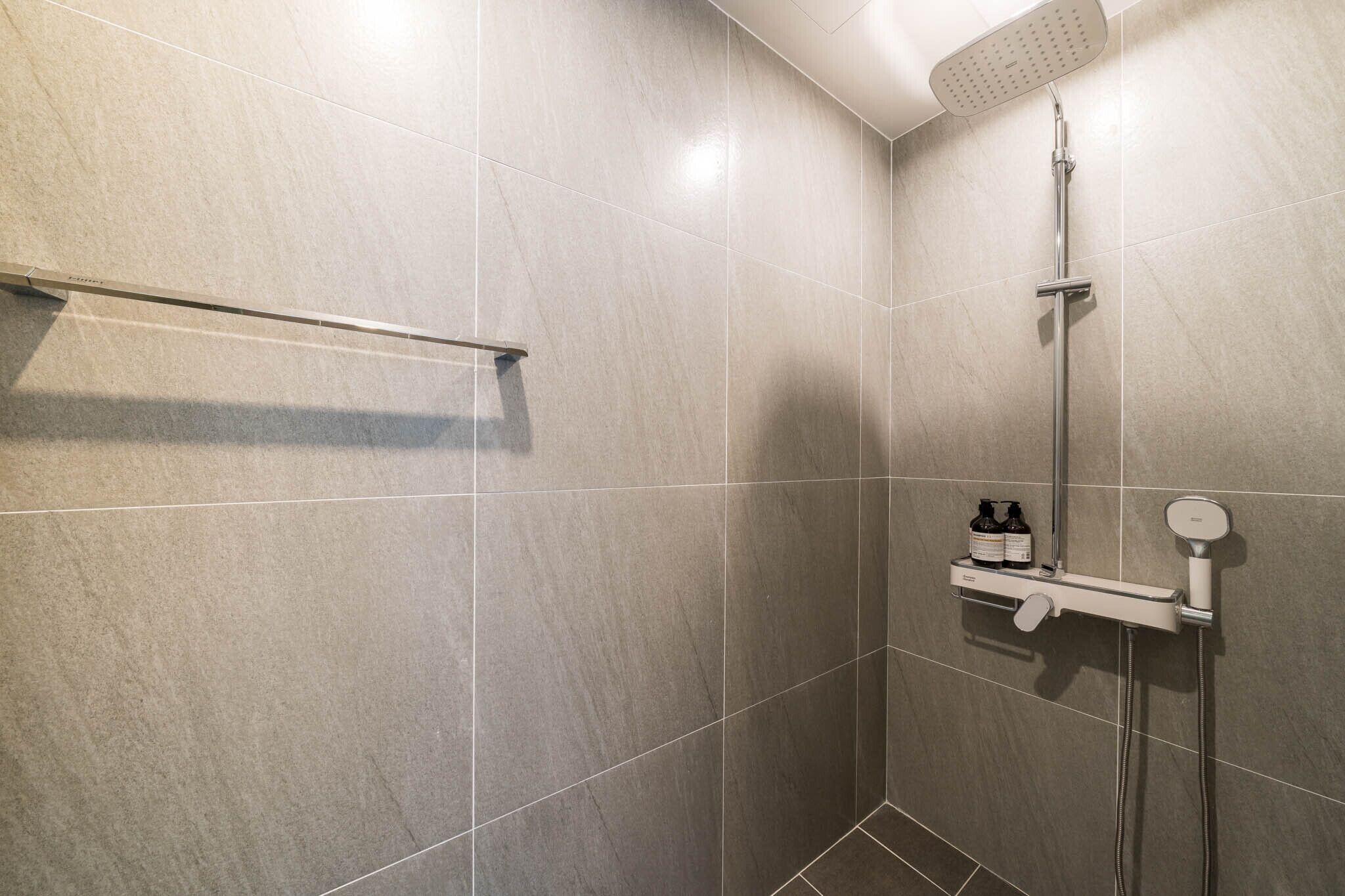 A modern shower area with a handheld showerhead, a wall-mounted shelf with toiletries, and a towel rack.
