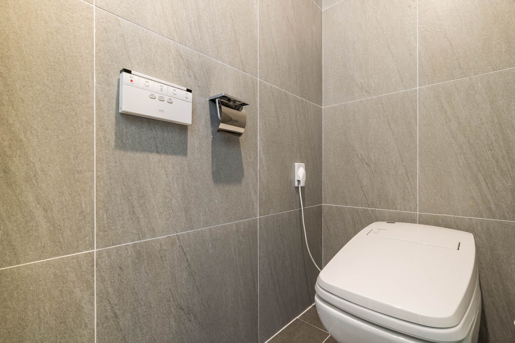 A modern bathroom with a toilet, a wall-mounted toilet paper holder, and a control panel.