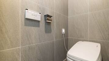 A modern bathroom with a toilet, a wall-mounted toilet paper holder, and a control panel.