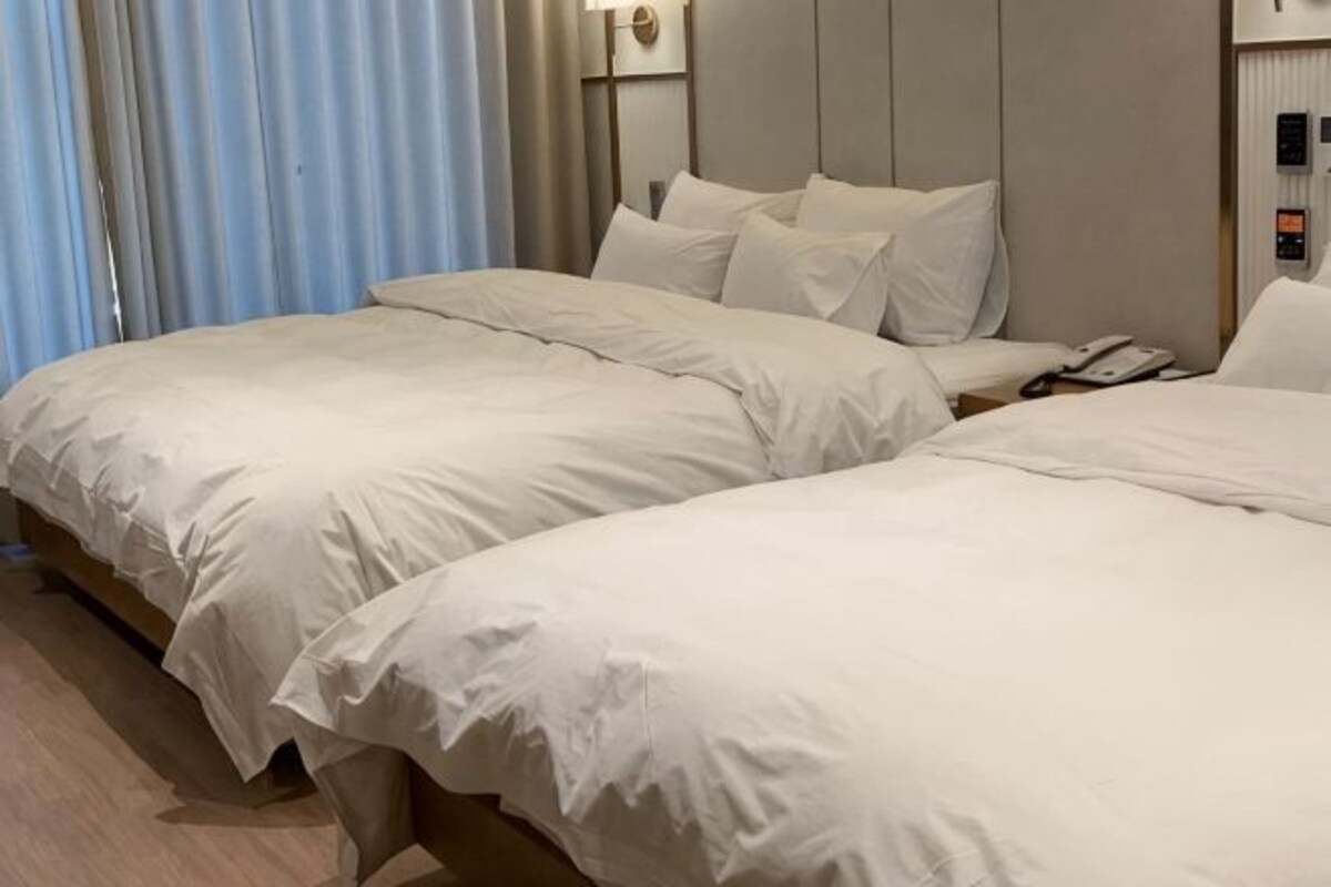 A hotel room with two beds, a nightstand, a phone, and a wall-mounted light fixture.
