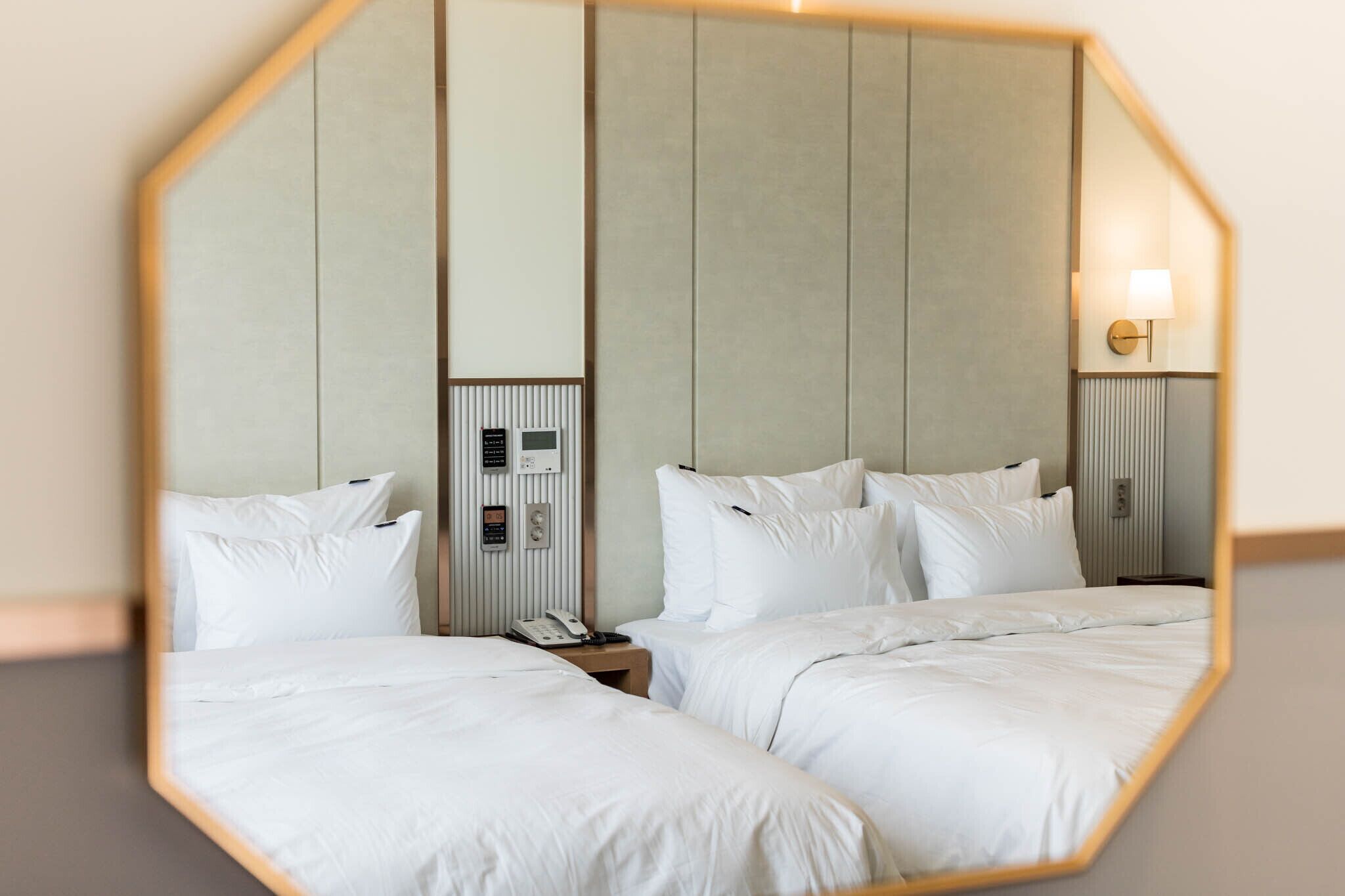 Habitación de hotel con dos camas, un espejo, una mesita de noche, un teléfono y una lámpara fijada a la pared.