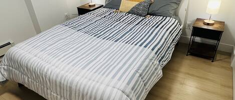 A bed with striped bedding, two bedside tables with lamps, and a wooden floor.