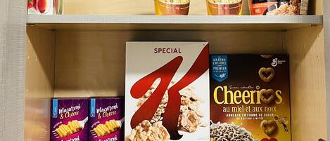 Un estante de la despensa repleto de diversos alimentos, como macarrones con queso, Cheerios y fideos instantáneos.