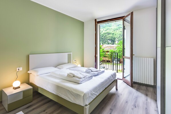 A bedroom with a bed, bedside table, and a view of a balcony.
