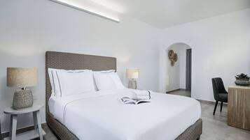 Una habitación de hotel moderna con una cama grande, dos mesitas de noche con lámparas, un escritorio pequeño y una planta en maceta.