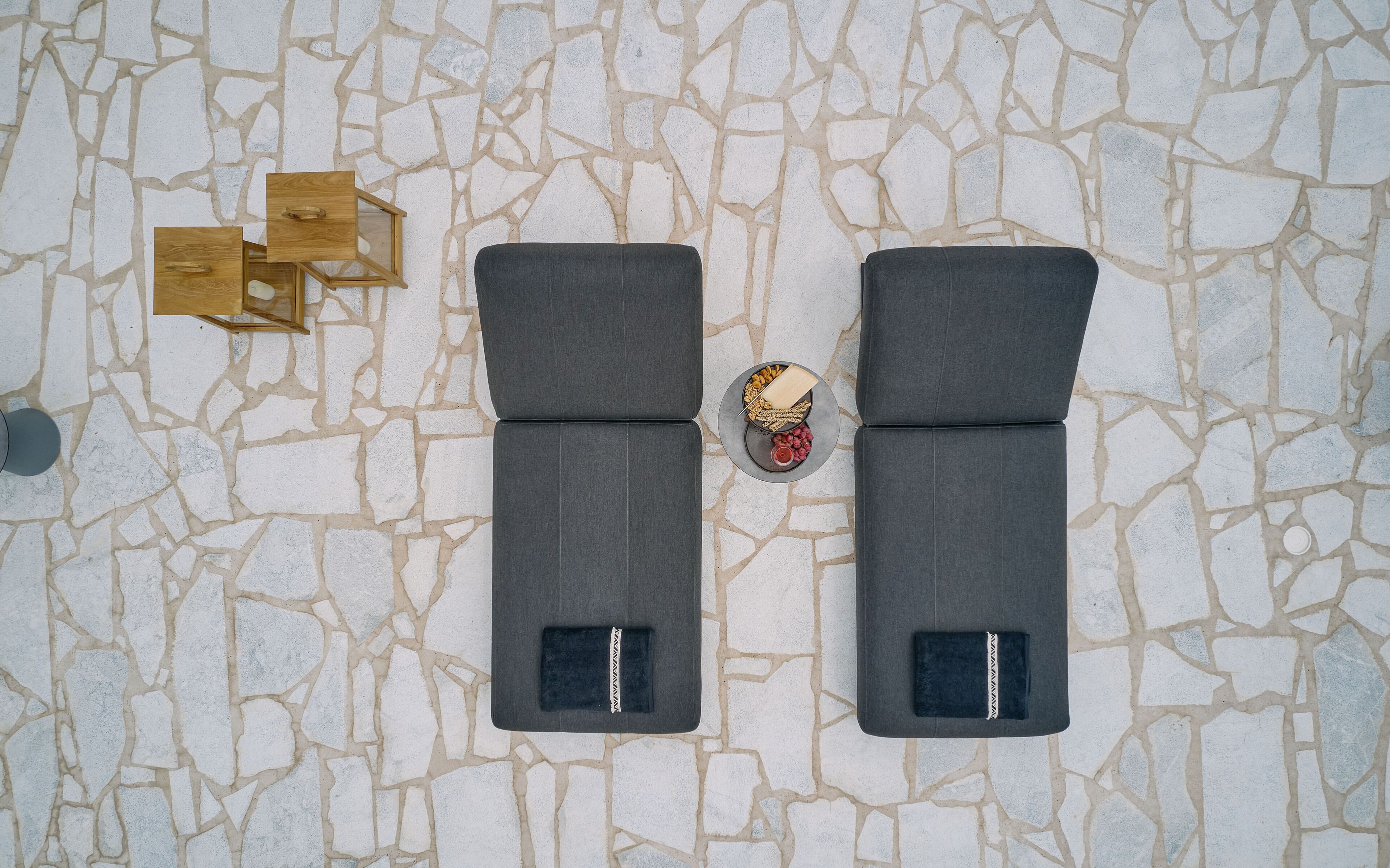 Dos sillones grises con compartimentos de almacenamiento, una mesita con bocadillos y una bebida, y un mueble de madera con espejo.