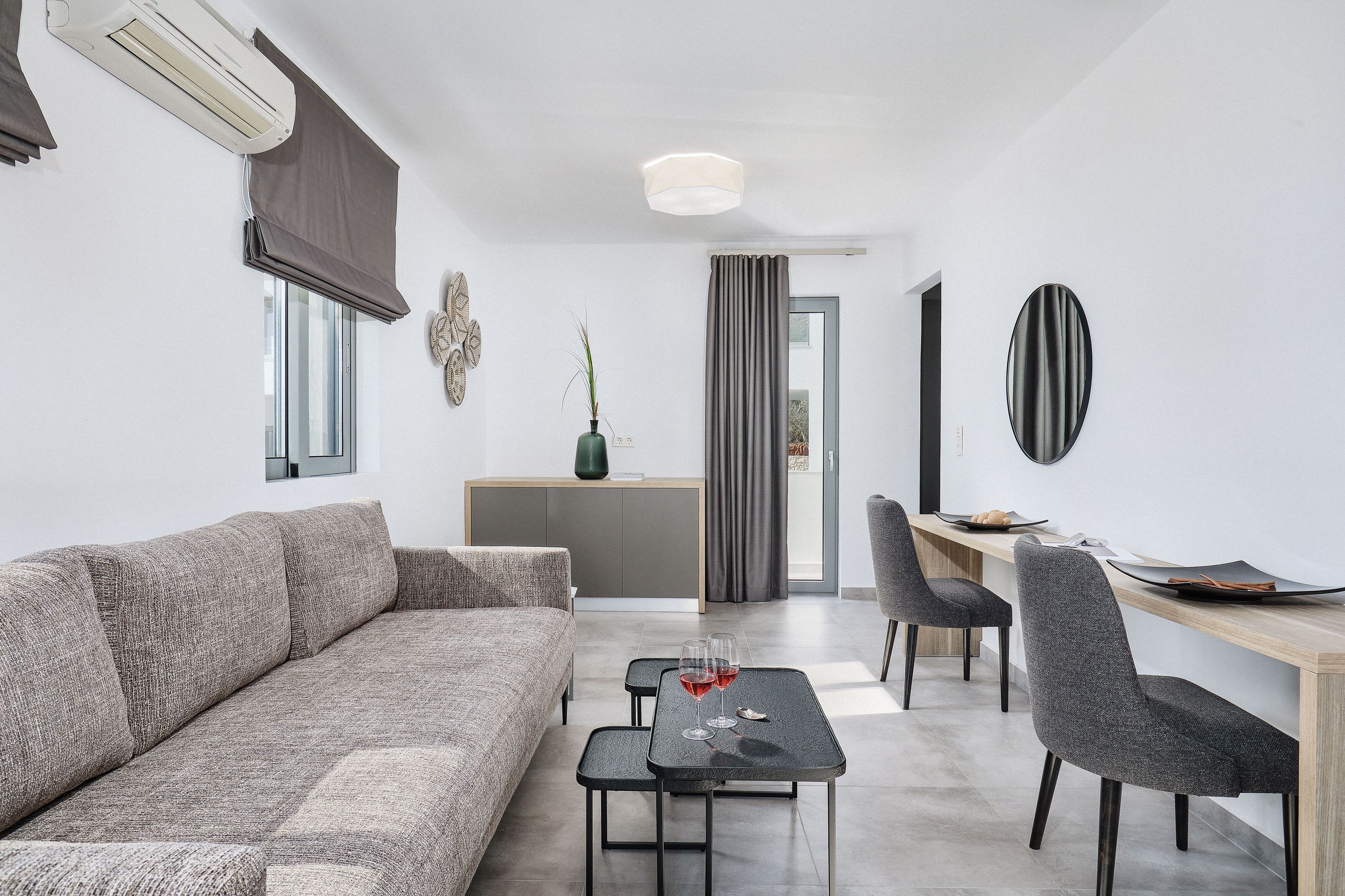 Een moderne woonkamer met een grijze bank, een klein bijzettafeltje met glazen, en een eethoek met een houten tafel en stoelen.