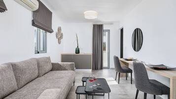 Een moderne woonkamer met een grijze bank, een klein bijzettafeltje met glazen, en een eethoek met een houten tafel en stoelen.