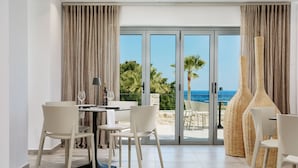 Un espace repas moderne avec une table et des chaises, une vue sur la mer à travers de grandes portes vitrées et un fauteuil en osier.