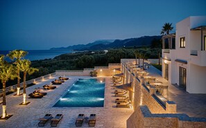 A poolside area with lounge chairs and a view of the sea and mountains. - Quattro Suites (Monemvasia)