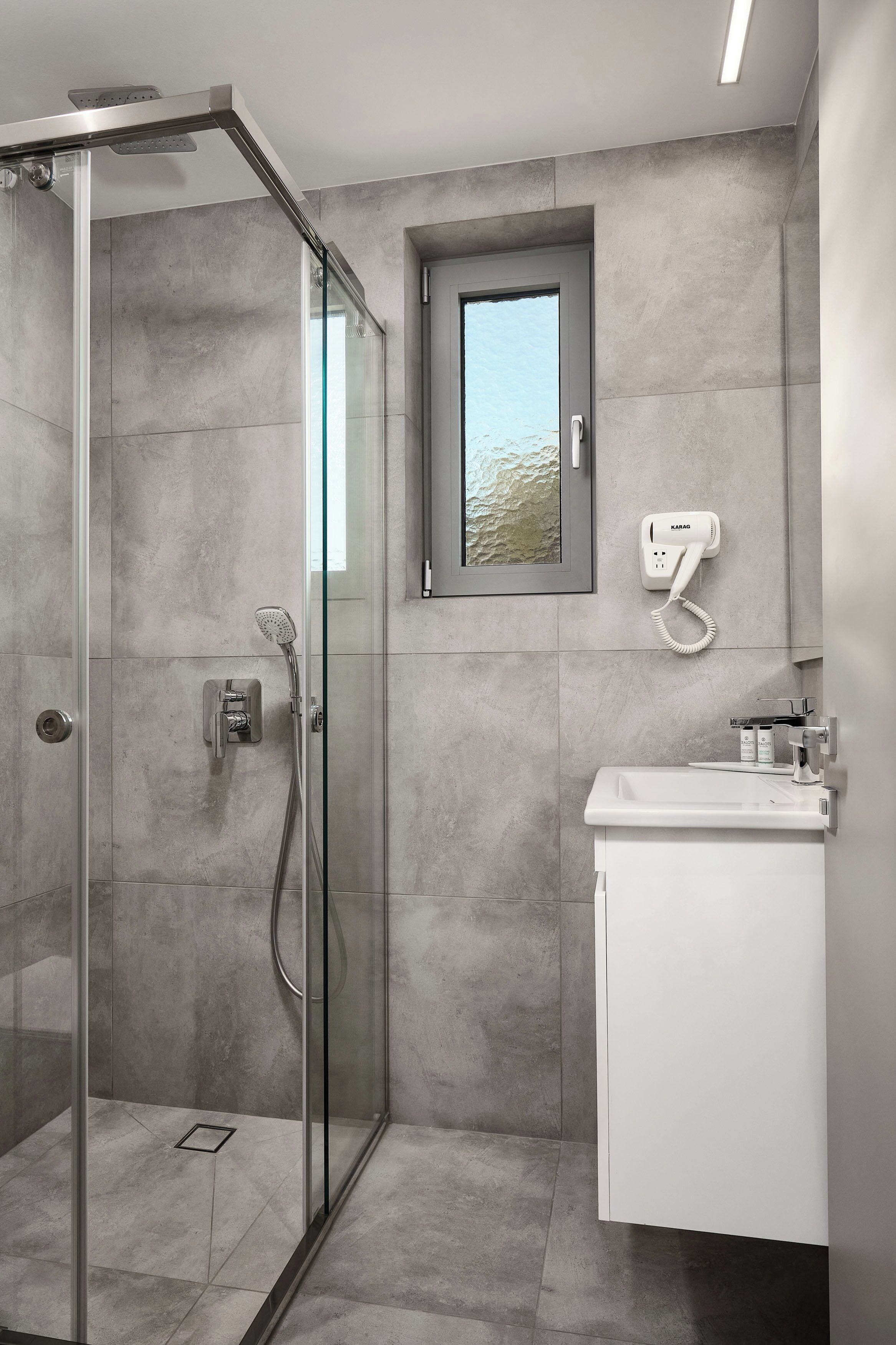 A modern bathroom with a glass-enclosed shower, a small window, and a hairdryer mounted on the wall.
