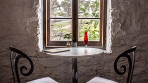 Una mesa con un florero y una copa, una planta pequeña y una ventana con vistas a la vegetación.