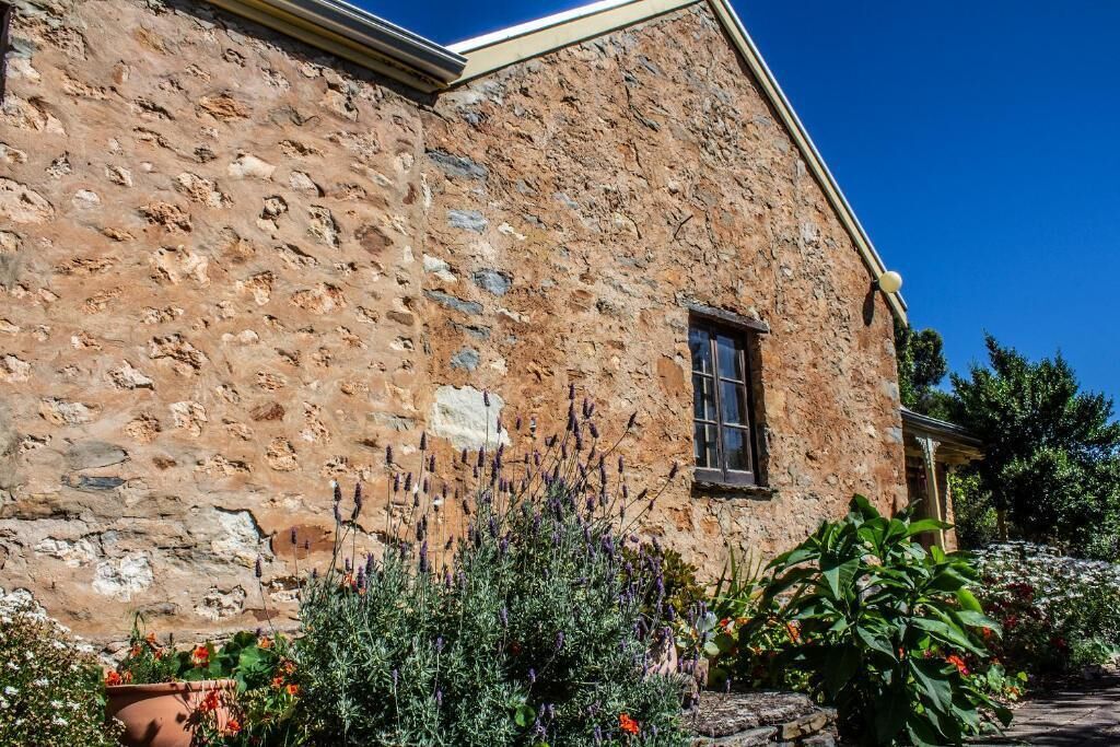 Ein Steinhaus mit Fenster und Tür, umgeben von verschiedenen Pflanzen und Blumen.
