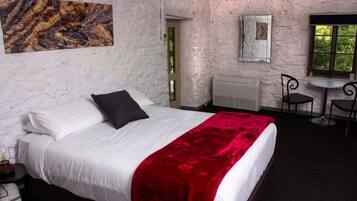 A bedroom with a bed, a red throw blanket, a white headboard, a nightstand, a mirror, a window, and a door.