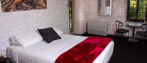 A bedroom with a bed, a red throw blanket, a white headboard, a nightstand, a mirror, a window, and a door.