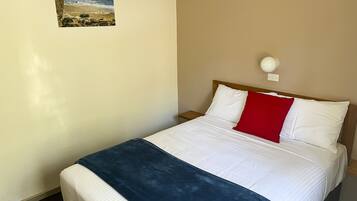 A hotel room with a bed, a nightstand, a wall-mounted lamp, and a picture of a beach scene.