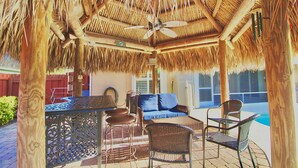 A covered outdoor seating area with a ceiling fan, wicker furniture, and a view of a swimming pool.