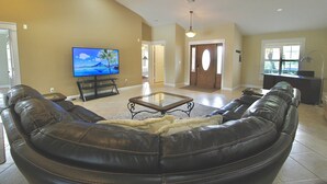 A living room with a leather sofa, a glass coffee table, a flat-screen TV, and a door leading to another room.