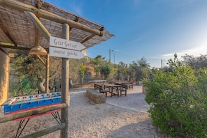 An outdoor seating area with tables and chairs, a foosball table, and a sign reading "barbecue parco giochi".