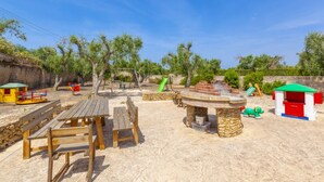 A sandy outdoor area with wooden benches, a stone fire pit, and a small play structure. - Cava Li Santi Residence - Monolocale 2 Int 10 (Santa Caterina)