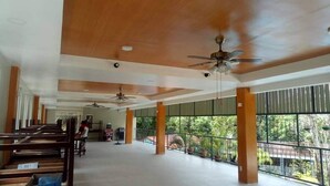 Un vaste espace intérieur doté de hauts plafonds, de plusieurs ventilateurs de plafond et de grandes fenêtres offrant une vue sur la verdure environnante.