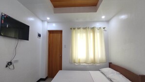 Une chambre à coucher avec un lit, un téléviseur fixé au mur, une porte en bois et une fenêtre avec des rideaux.