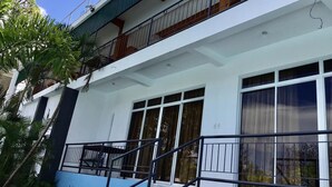 Un immeuble de deux étages doté d’un balcon à l’étage supérieur, de grandes fenêtres et d’un escalier menant à l’entrée.