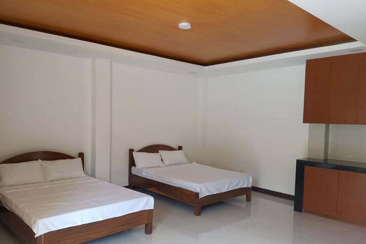 A room with two wooden beds, white bedding, a wooden ceiling, and a built-in cabinet.