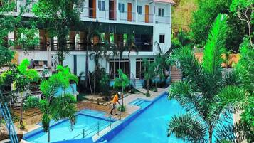 Un resort con varias piscinas, un edificio grande con balcones y abundante vegetación.