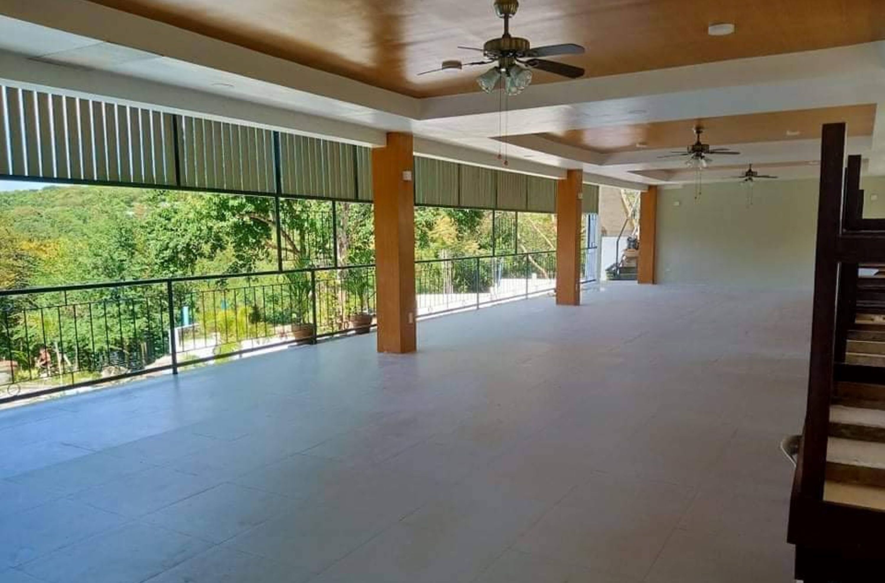 A spacious indoor area with large windows, ceiling fans, and a balcony with a railing.