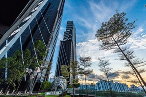 A modern urban landscape with high-rise buildings, a prominent curved skyscraper, and a well-maintained park area with trees and a decorative metal sculpture. - Instagrammable Arte Mont Kiara 2 Rooms (Kuala Lumpur)