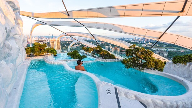 A man taking a photo in a large, curved pool with a cityscape in the background. - Instagrammable Arte Mont Kiara 2 Rooms (Kuala Lumpur)