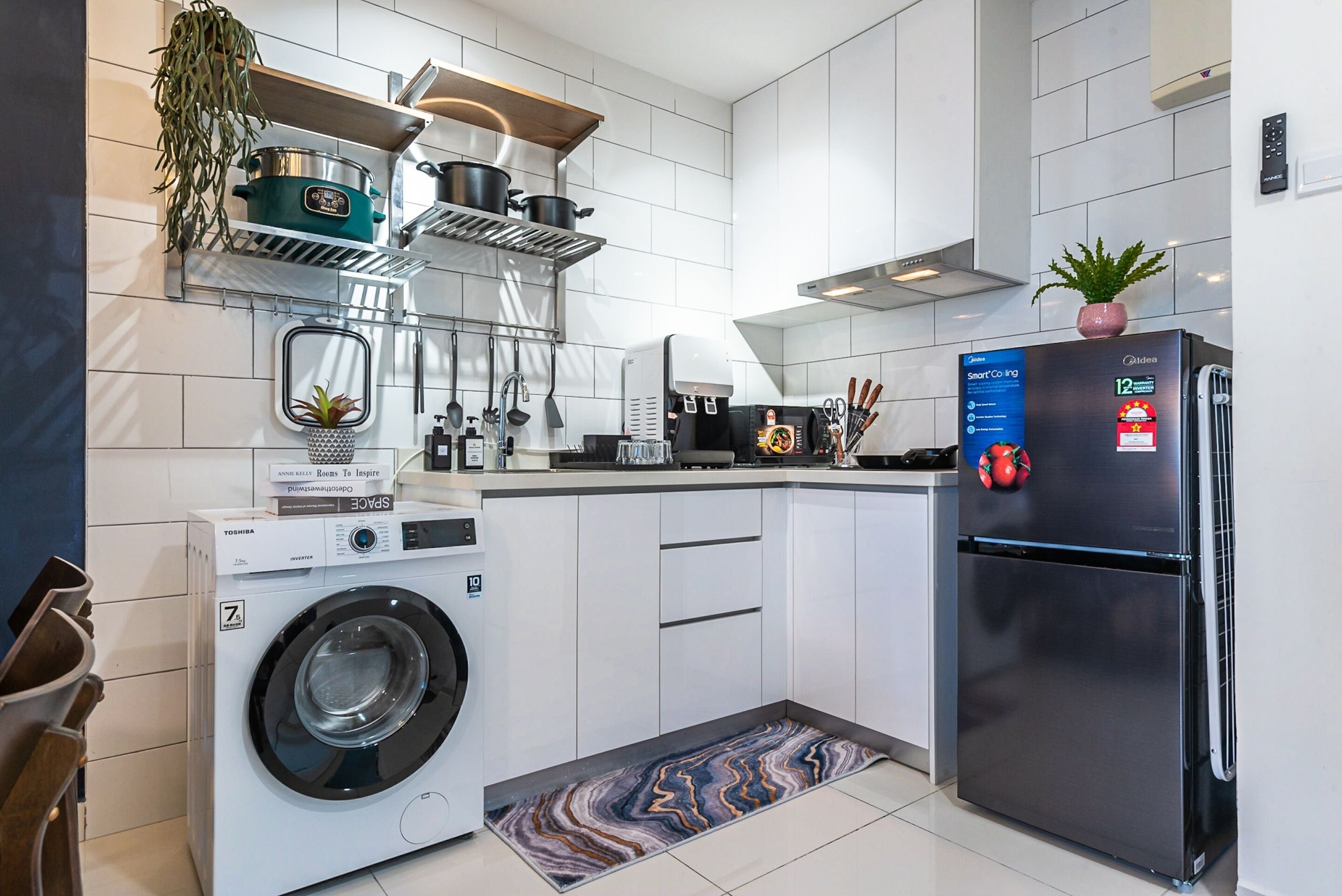 A modern kitchen with white cabinets, a stainless steel refrigerator, a washing machine, and a countertop with a coffee maker and a plant.