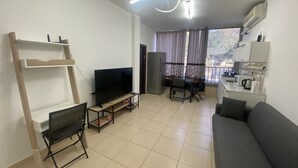 Una sala moderna con un televisor de pantalla plana, un sofá, una mesa de comedor con sillas y una cocina con microondas.