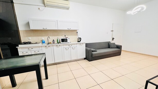 Una cocina moderna con armarios blancos, un sofá gris y una mesa de comedor.