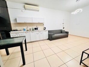 A modern kitchen with white cabinets, a grey sofa, and a dining table.