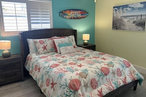 A bedroom with a bed, a nightstand, a lamp, a window with blinds, and wall art.