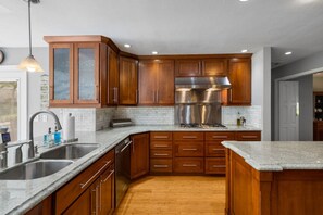 A kitchen with wooden cabinets, a stainless steel range hood, a granite countertop, and a wooden floor. - 201 S berry  · lNDOOR POOL! The FUN house (Rapid City)