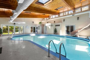 An indoor swimming pool with a slide, wooden ceiling, and large windows. - 201 S berry  · lNDOOR POOL! The FUN house (Rapid City)