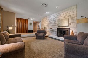 A living room with a fireplace, a stone wall, and a sofa. - 201 S berry  · lNDOOR POOL! The FUN house (Rapid City)