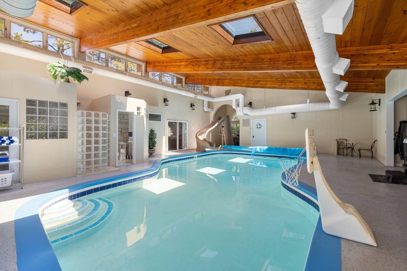 An indoor swimming pool with a slide, wooden ceiling, and a view of the outdoors.
