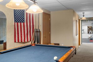 Ein Billardtisch mit amerikanischer Flagge, Billardstöcken und einer Tür in einem Raum mit Teppichboden und Deckenleuchten.