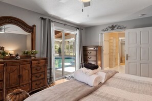 Ein Schlafzimmer mit Bett, Schminktisch, Spiegel und Blick auf einen Swimmingpool.