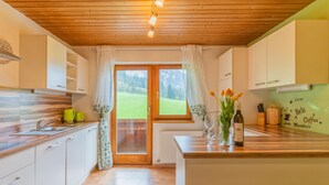 A modern kitchen with white cabinets, a wooden countertop, and a view of a green landscape through a glass door.