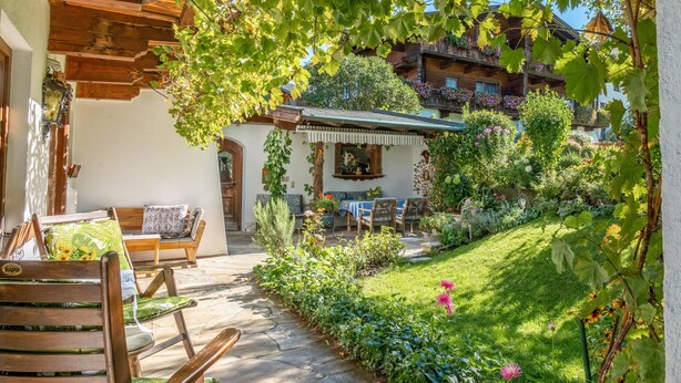 A rustic wooden building with a covered patio, stone flooring, and a garden with various plants and flowers.