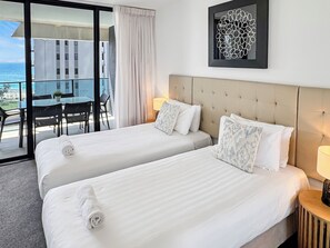 Une chambre d’hôtel avec deux lits, un balcon doté d’une table et de chaises, et une vue sur l’océan.
