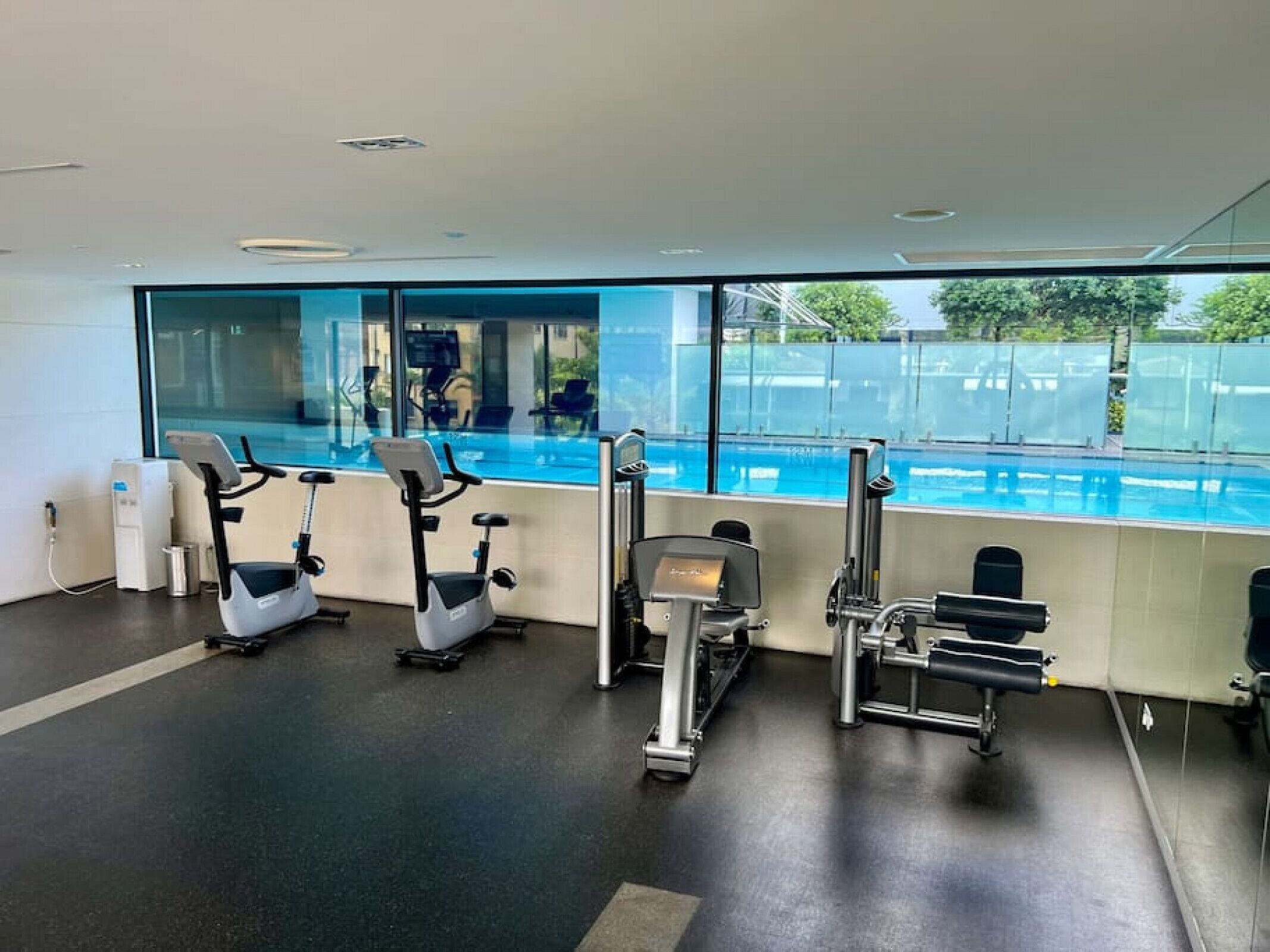 A gym with cardio machines, weight equipment, and a large window overlooking a pool.