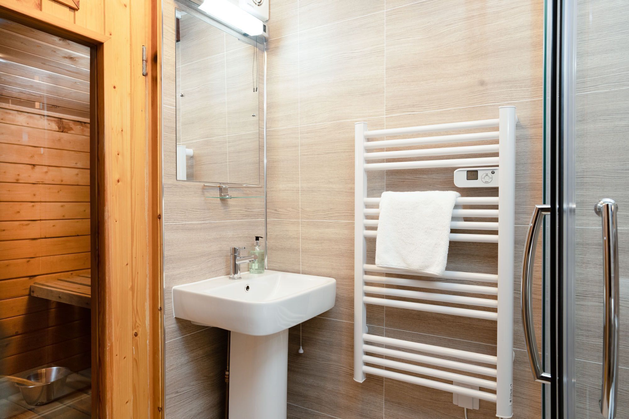 A bathroom with a wooden floor, a white sink, a glass shower enclosure, and a towel rack with a white towel.