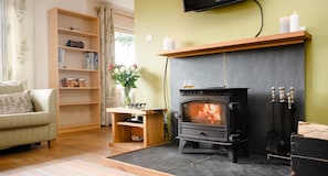 A cozy living room with a fireplace, a sofa, a bookshelf, and a vase with flowers.